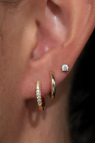 Model wearing a coordinated earring stack featuring gold-tone huggie hoop earrings with sparkling crystal accents, polished gold-tone huggie hoops, and round crystal stud earrings. 