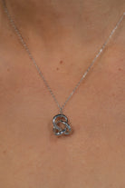Close up of model wearing a delicate silver-tone necklace featuring an interlocking infinity knot pendant suspended from a fine chain. The minimalist design sits at the collarbone for an elegant, everyday look.