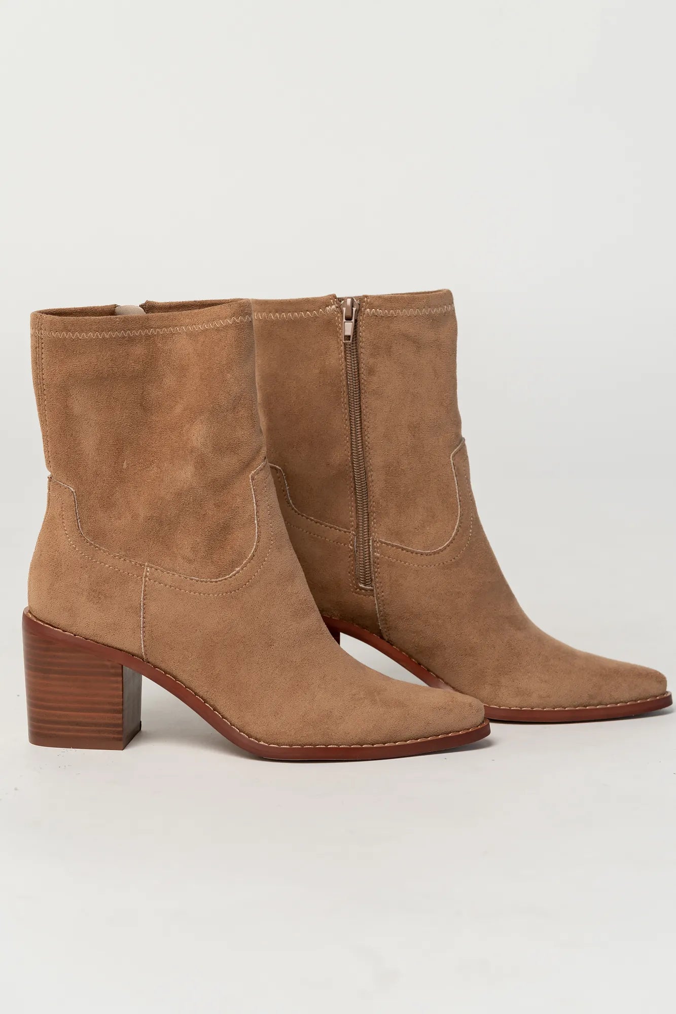 Pair of sand-colored ankle boots featuring a soft suede-like finish, pointed toe silhouette, and stacked block heel. The boots include a side zipper closure and subtle western-inspired seam detailing, creating a versatile look that pairs easily with denim, dresses, and seasonal outfits.