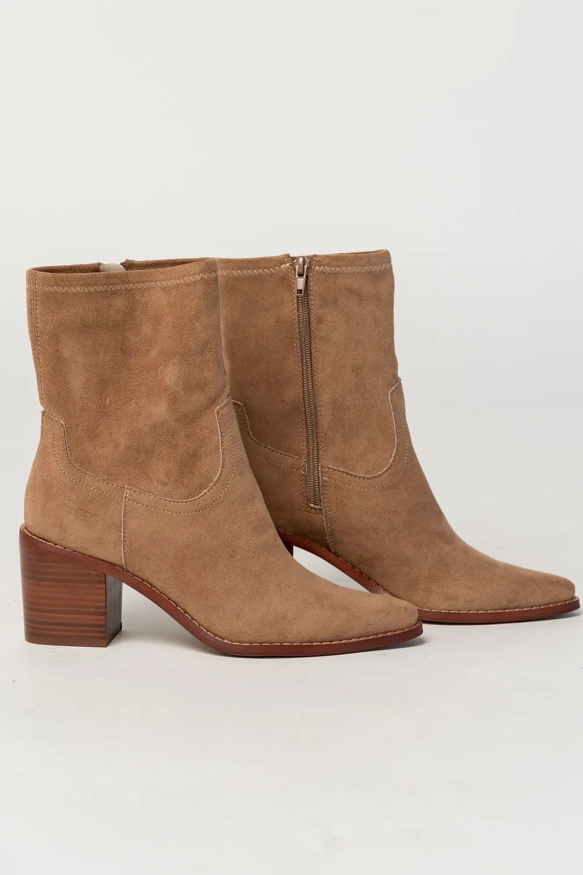 Pair of sand-colored ankle boots featuring a soft suede-like finish, pointed toe silhouette, and stacked block heel. The boots include a side zipper closure and subtle western-inspired seam detailing, creating a versatile look that pairs easily with denim, dresses, and seasonal outfits.