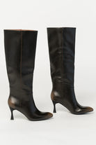 Pair of black knee-high boots featuring a pointed toe, sleek fitted shaft, and sculpted kitten heel. The streamlined silhouette and smooth finish create an elegant, versatile look that pairs effortlessly with dresses, skirts, and tailored outfits.