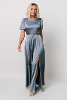 Styled shot of the Agnes Satin Maxi Dress in whisper blue paired with heels, showing overall silhouette, flutter sleeves, and maxi-length sweep.