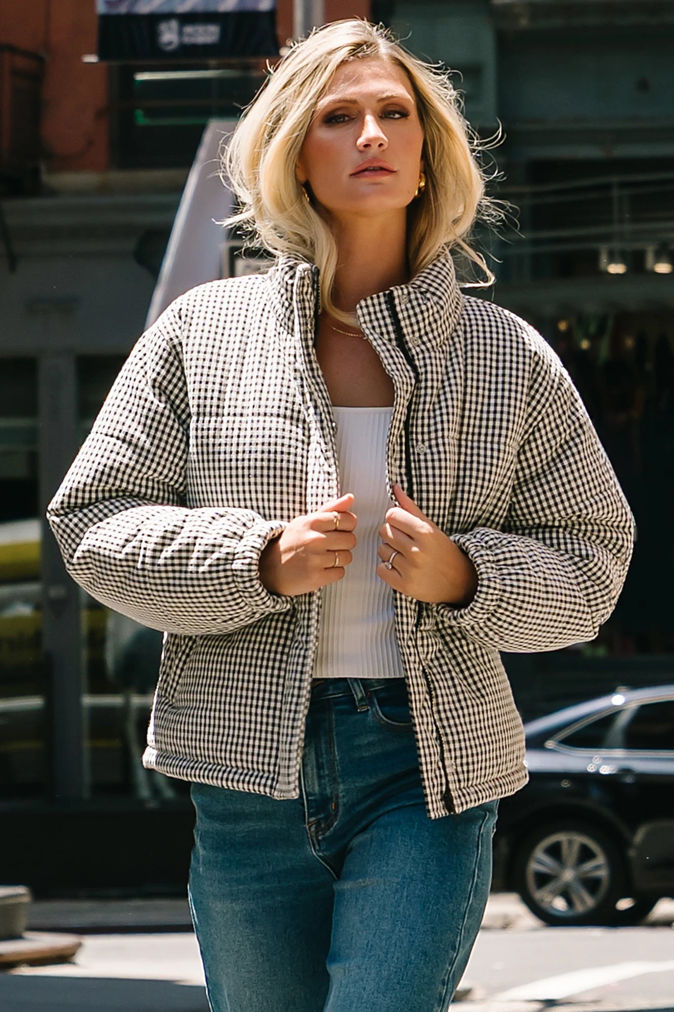 Model wearing the Vivienne Coat featuring a black and white gingham quilted puffer design with a high collar, front zipper and snap-button closure, long sleeves, and a relaxed silhouette.