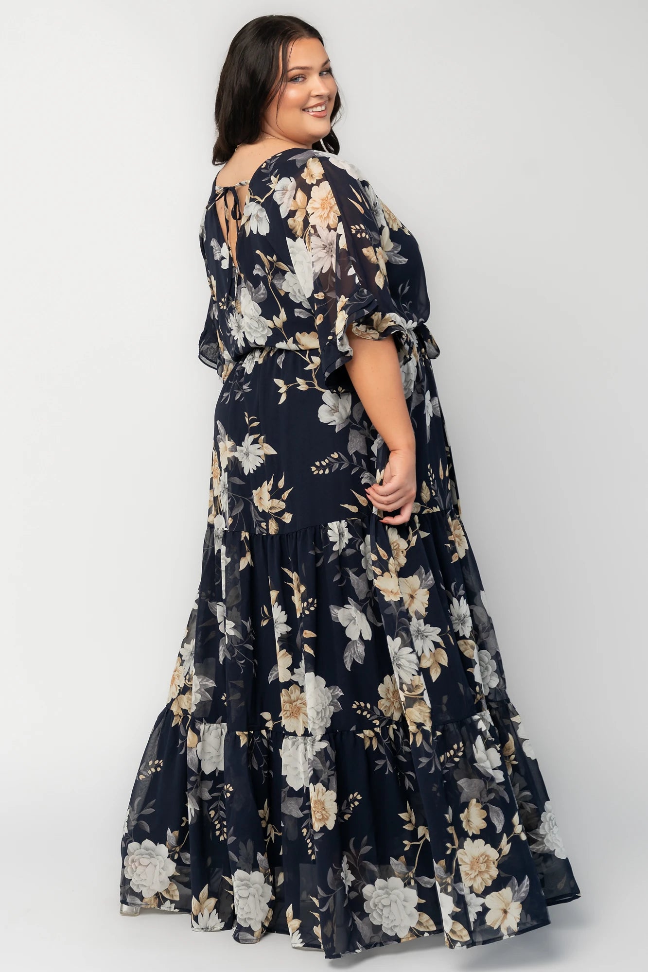 Model wearing the Luna Maxi Dress in Navy Floral featuring a surplice V-neckline with a V-back and tie detail, soft flutter sleeves, and an elastic waist with a removable sash tie