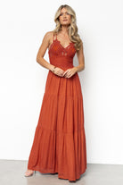 Full-length image of rust lace top maxi dress on model walking outdoors, highlighting flow of tiered skirt and textured bodice.