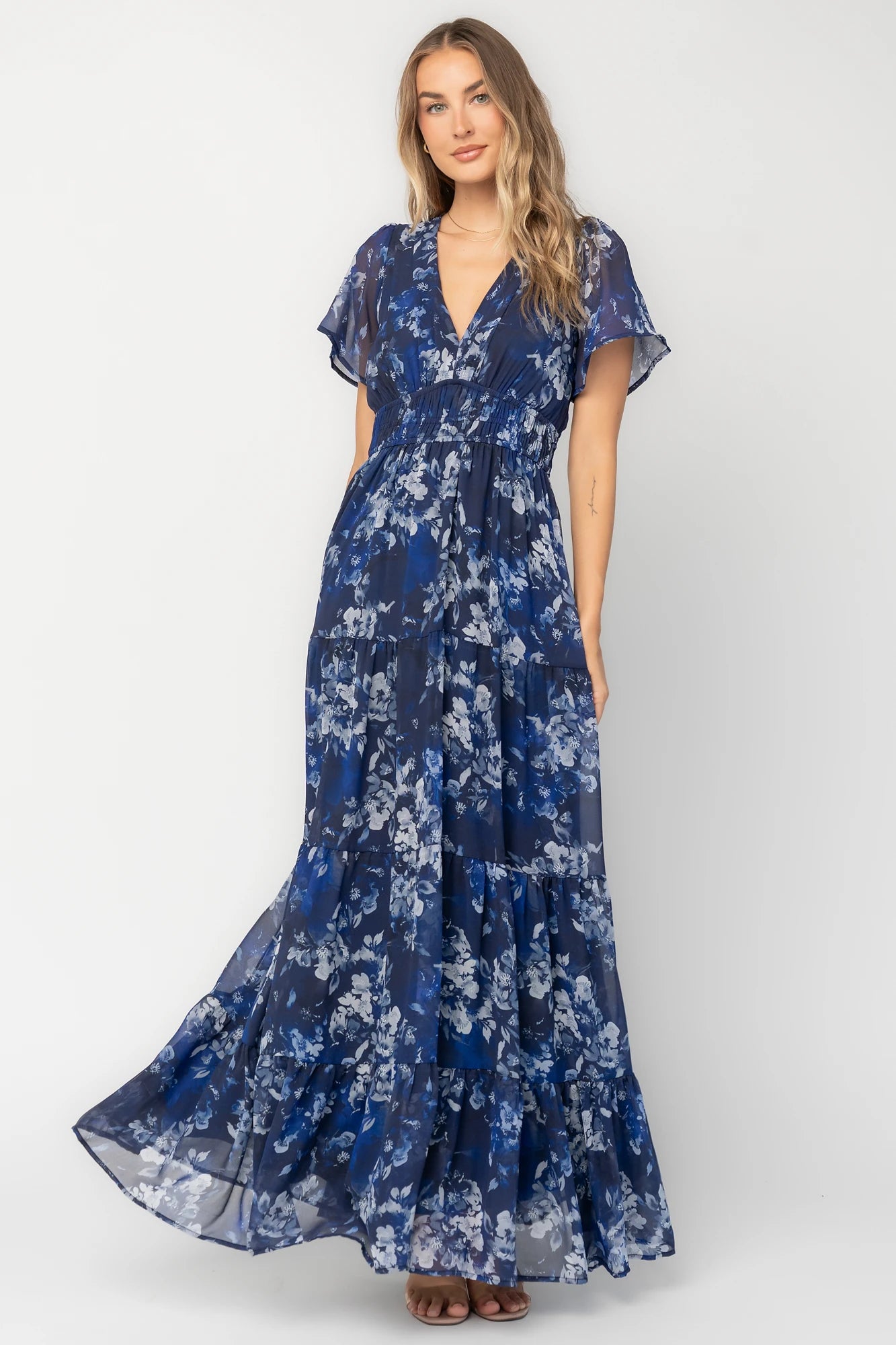 Blue floral chiffon maxi dress with flutter sleeves, surplice V-neck, smocked elastic waist, tiered skirt, and lined body.