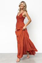Model seated in rust lace-bodice maxi dress highlighting relaxed drape, tiered skirt movement, and lightweight woven fabric.