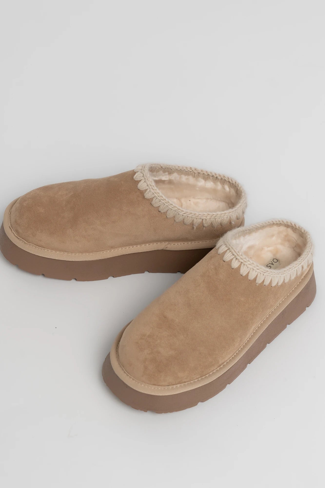 Tan platform mule slippers with a faux suede upper, plush faux fur lining, whipstitch trim, and cushioned slip-on design.