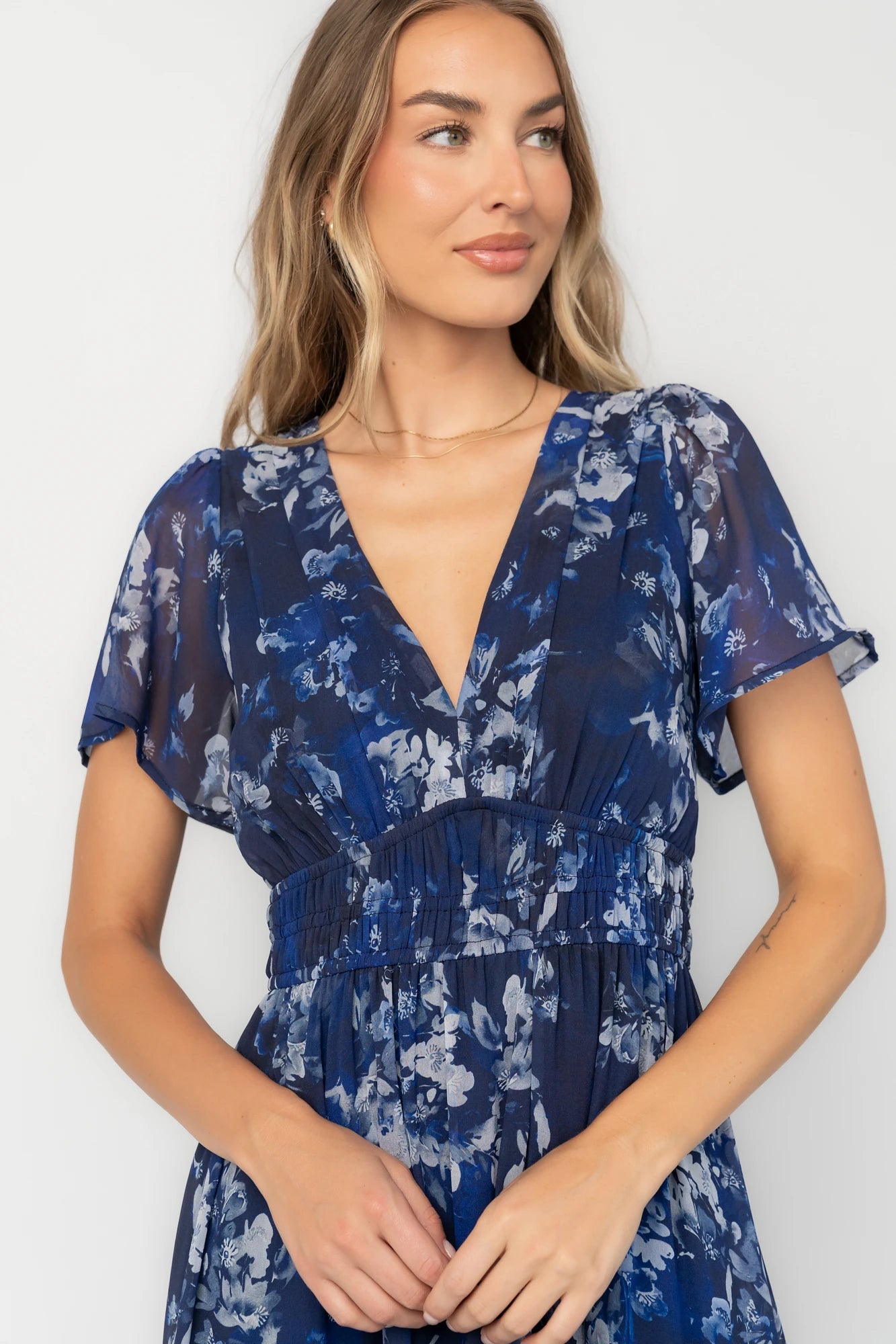Blue floral chiffon maxi dress with flutter sleeves, surplice V-neck, smocked elastic waist, tiered skirt, and lined body.