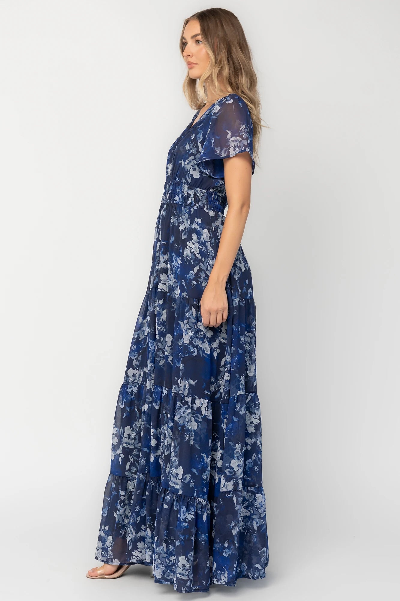 Blue floral chiffon maxi dress with flutter sleeves, surplice V-neck, smocked elastic waist, tiered skirt, and lined body.