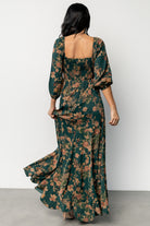 Model wearing green and copper floral maxi dress walking to show godet hem flare and hemline length.