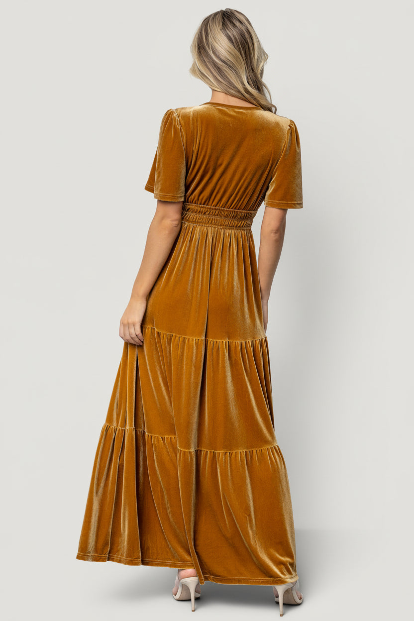 Styled editorial shot of the dark-gold Artemis dress paired with subtle accessories, demonstrating how the velvet gown photographs in event lighting.