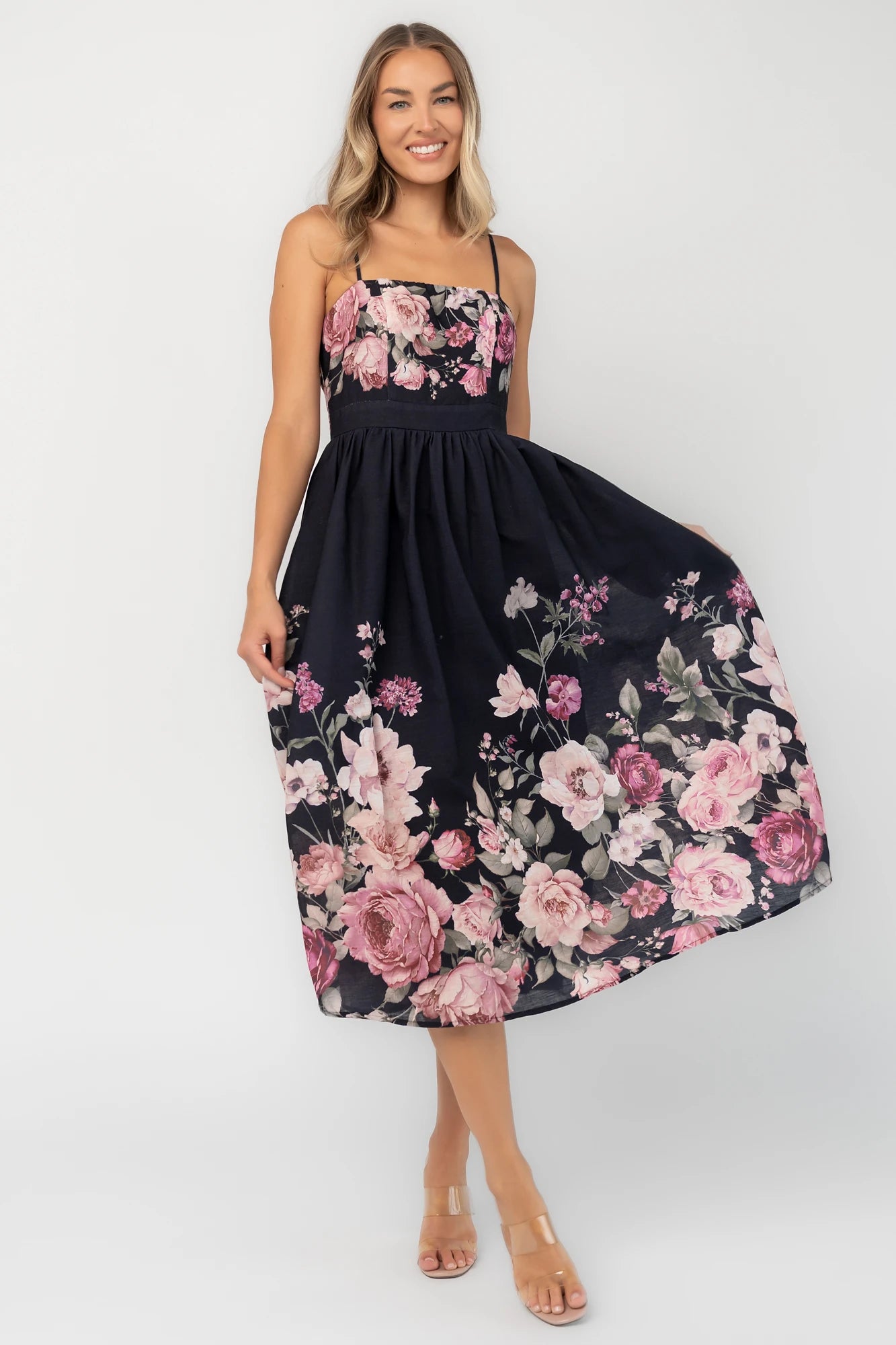 Black floral midi dress with a straight neckline, adjustable spaghetti straps, smocked back, gathered skirt, and side pockets.