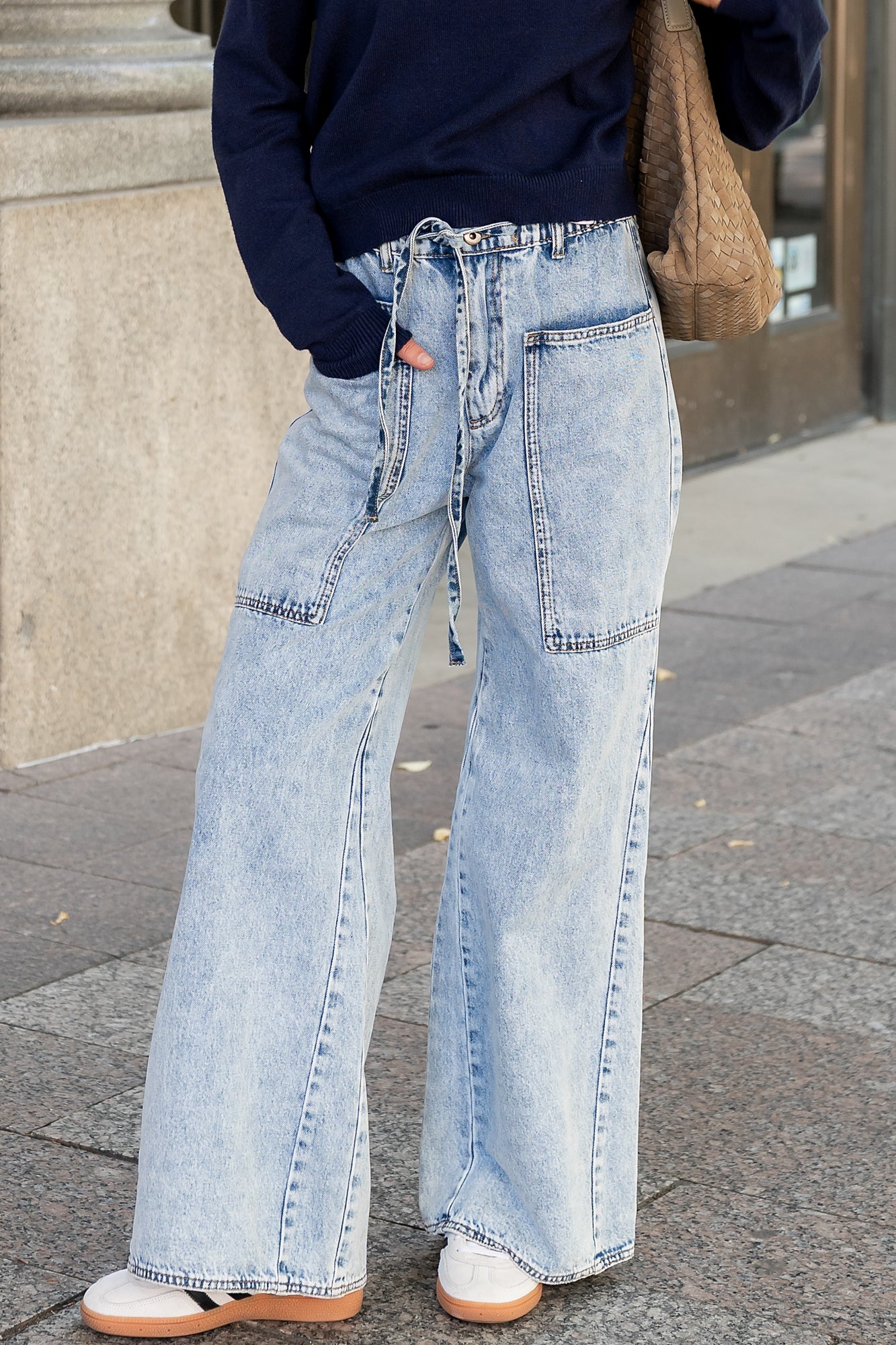 Front view of light wash wide-leg jeans on a model, showing elastic drawstring waistband, oversized front pockets, and split outseam detail.