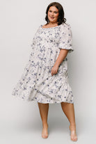 Full-length image of Marta Smocked Midi Dress in white and blue floral, styled with low heels for a spring event outfit.