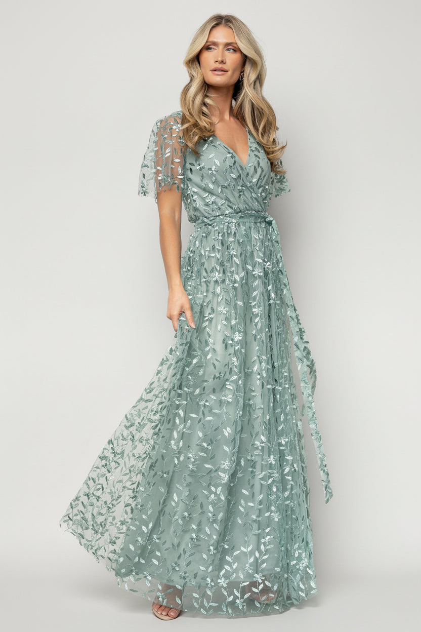 Front view of eucalyptus-green maxi dress with vine-embossed organza overlay, crossover surplice neckline, elastic waist, and left-side slit for movement.