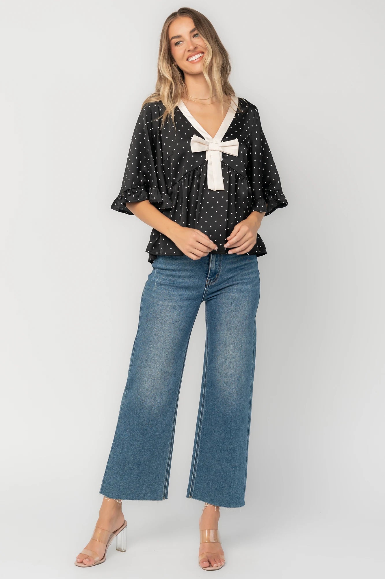 Black satin polka dot peplum top with an ivory contrast collar, decorative bow, V-neckline, and elbow-length ruffle sleeves.
