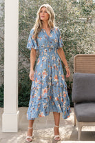 Front view of blue midi dress with peach floral print, V-neckline with ties, smocked waist, and lightweight rayon drape on model.