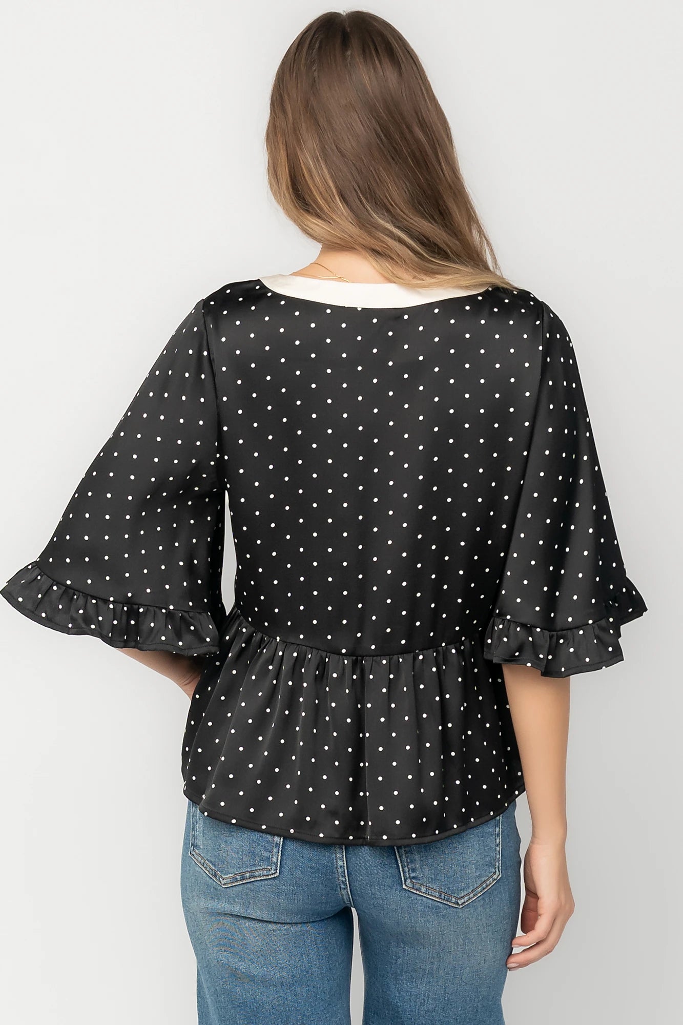 Black satin polka dot peplum top with an ivory contrast collar, decorative bow, V-neckline, and elbow-length ruffle sleeves.
