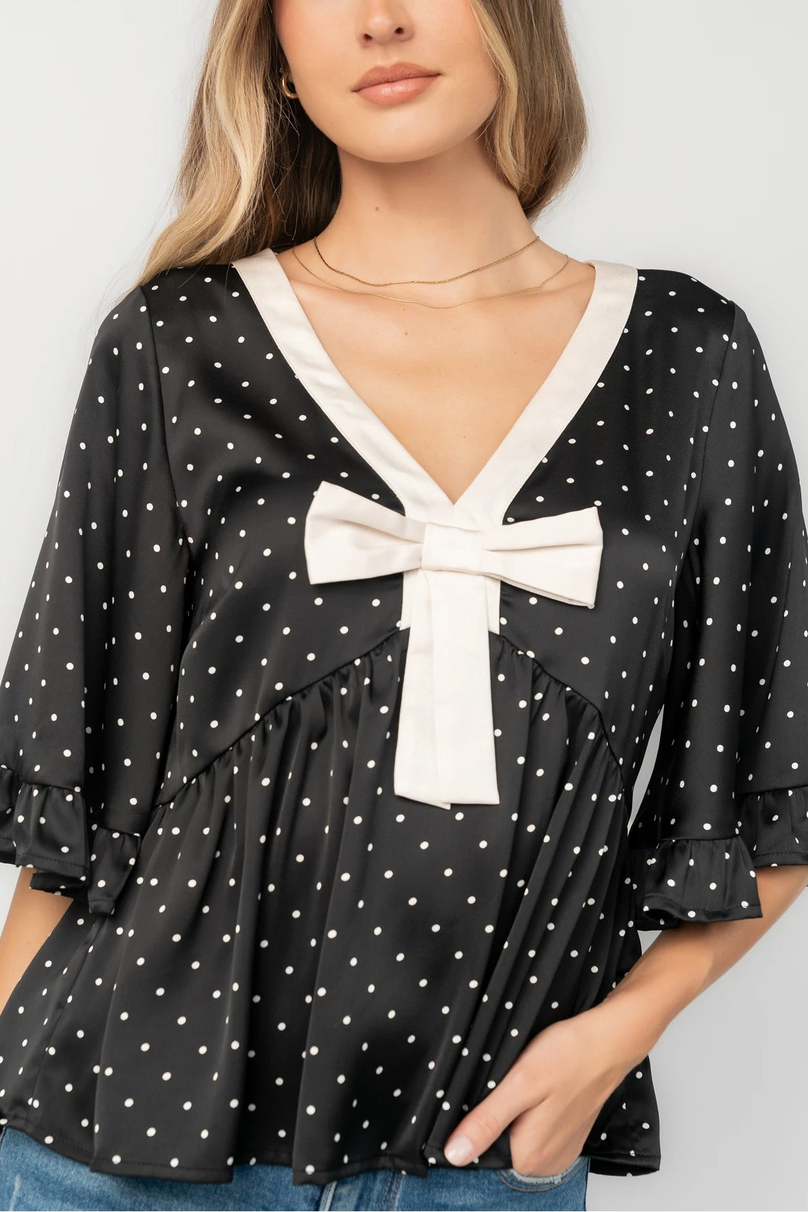 Black satin polka dot peplum top with an ivory contrast collar, decorative bow, V-neckline, and elbow-length ruffle sleeves.