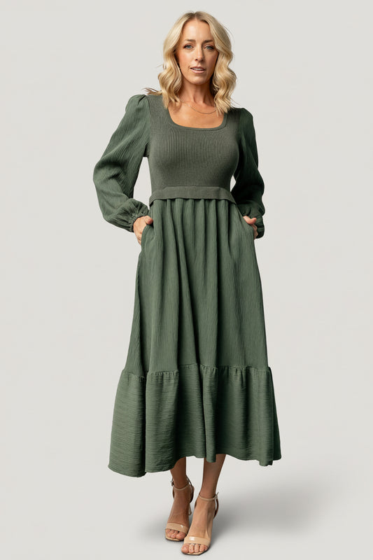Front view of model wearing dusty-green two-tone Alva sweater dress showing ribbed bodice, square neckline, ruffle shoulder, and midi hem.