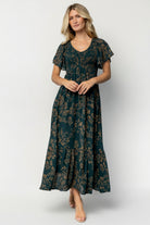 Front view of the Monica Smocked Maxi Dress in Deep Topaz with gold print on a model, showing V-neck, smocked bodice, and flowing maxi skirt.