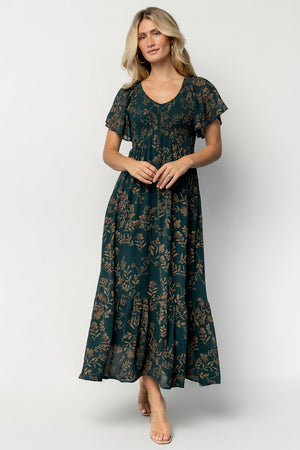Front view of the Monica Smocked Maxi Dress in Deep Topaz with gold print on a model, showing V-neck, smocked bodice, and flowing maxi skirt.
