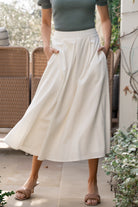 Model wearing off-white pleated midi skirt, front view showing high-rise waistband, flowing pleats, and subtle fabric texture across the skirt.