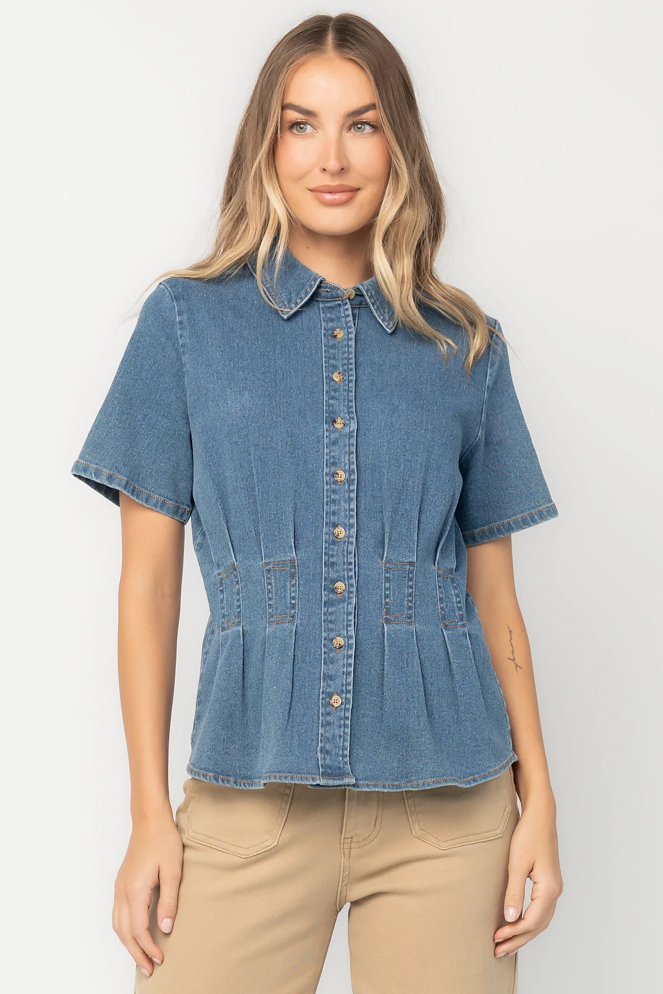 Medium wash stretch denim peplum top with a collared neckline, button-front closure, short sleeves, tailored seam detailing, and a flattering fitted silhouette.