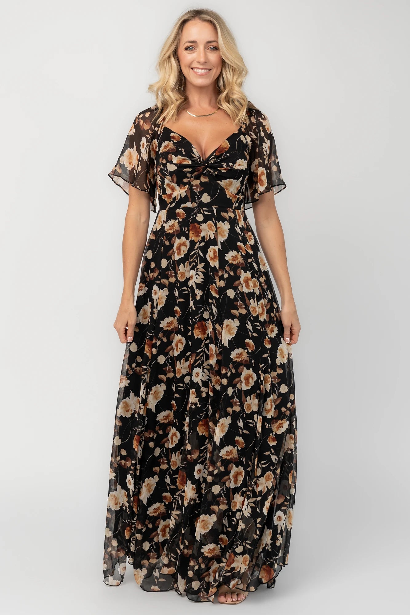 Black floral chiffon maxi dress with a sweetheart neckline, flutter sleeves, smocked back bodice, tiered skirt, and subtle gold foil detailing.
