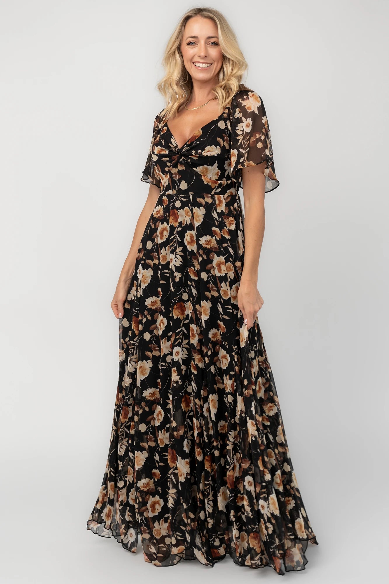 Black floral chiffon maxi dress with a sweetheart neckline, flutter sleeves, smocked back bodice, tiered skirt, and subtle gold foil detailing.
