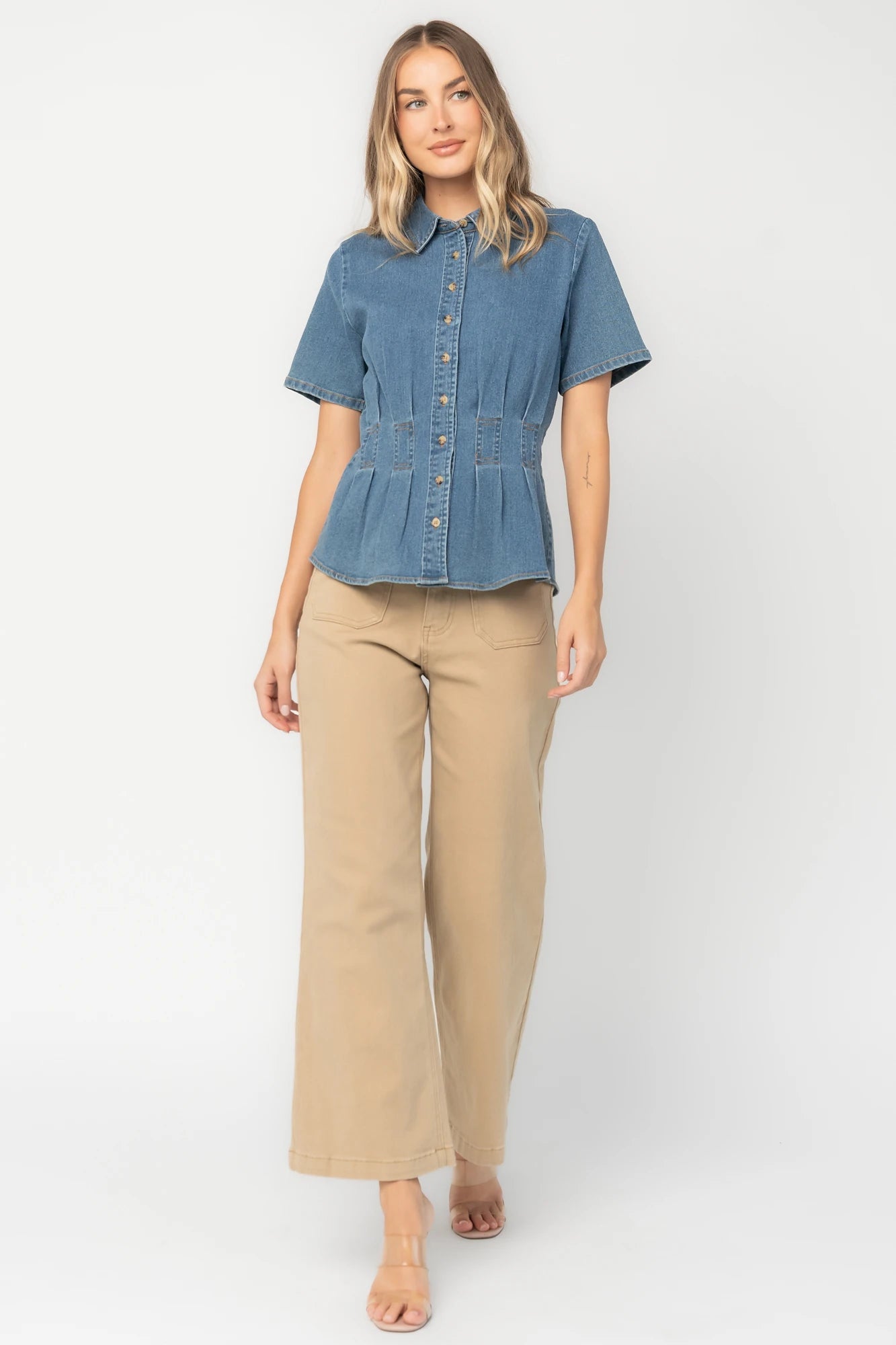 Medium wash stretch denim peplum top with a collared neckline, button-front closure, short sleeves, tailored seam detailing, and a flattering fitted silhouette.