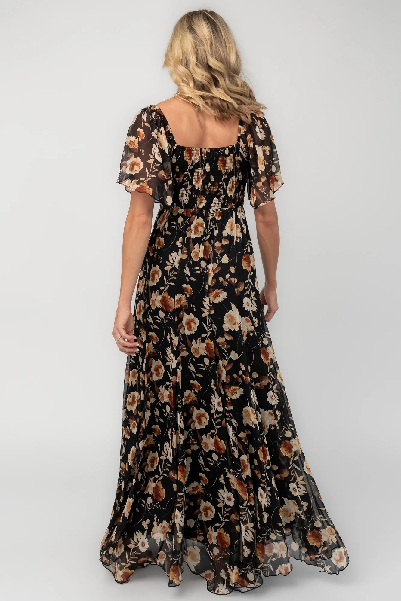 Black floral chiffon maxi dress with a sweetheart neckline, flutter sleeves, smocked back bodice, tiered skirt, and subtle gold foil detailing.