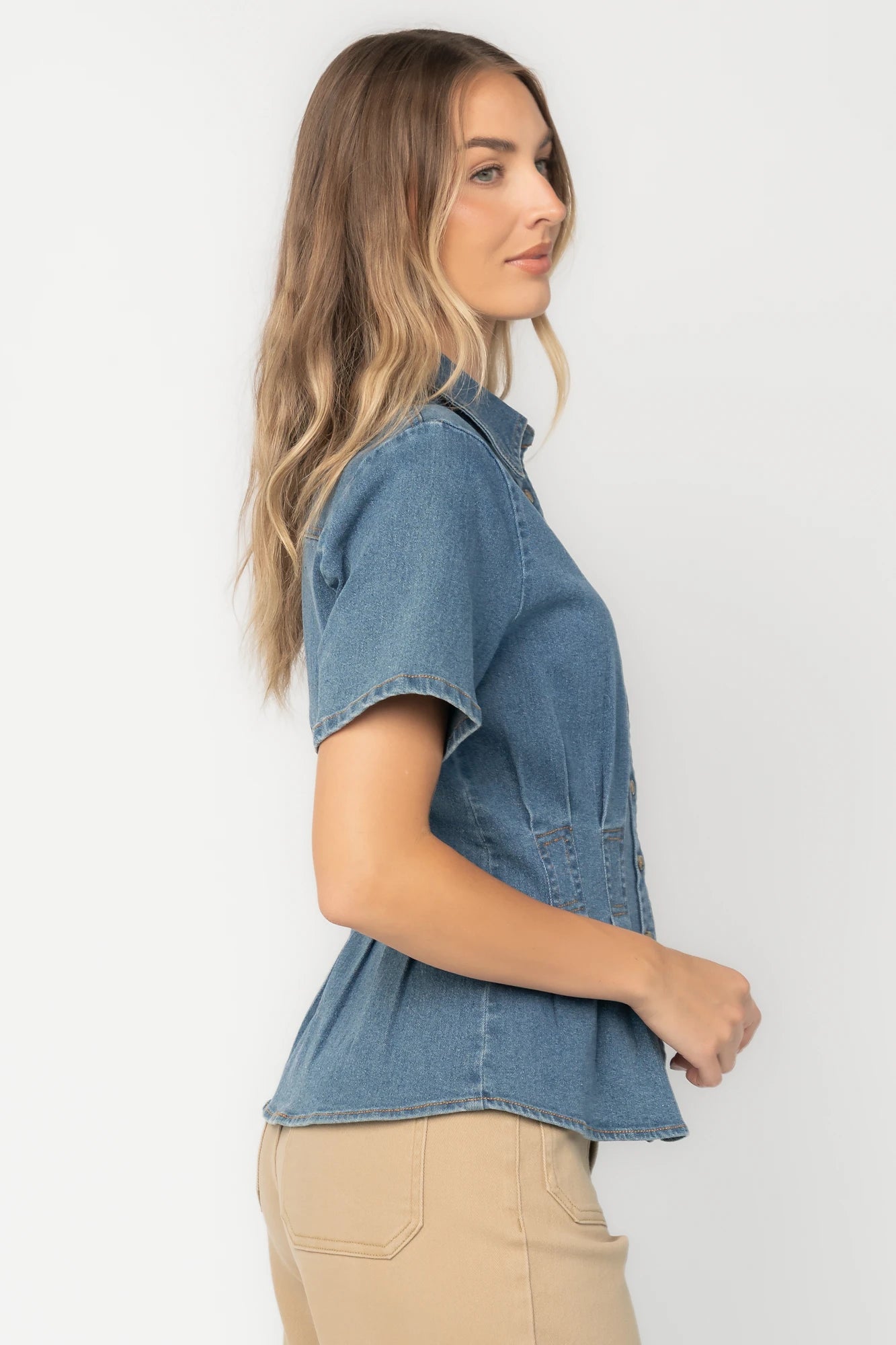 Medium wash stretch denim peplum top with a collared neckline, button-front closure, short sleeves, tailored seam detailing, and a flattering fitted silhouette.