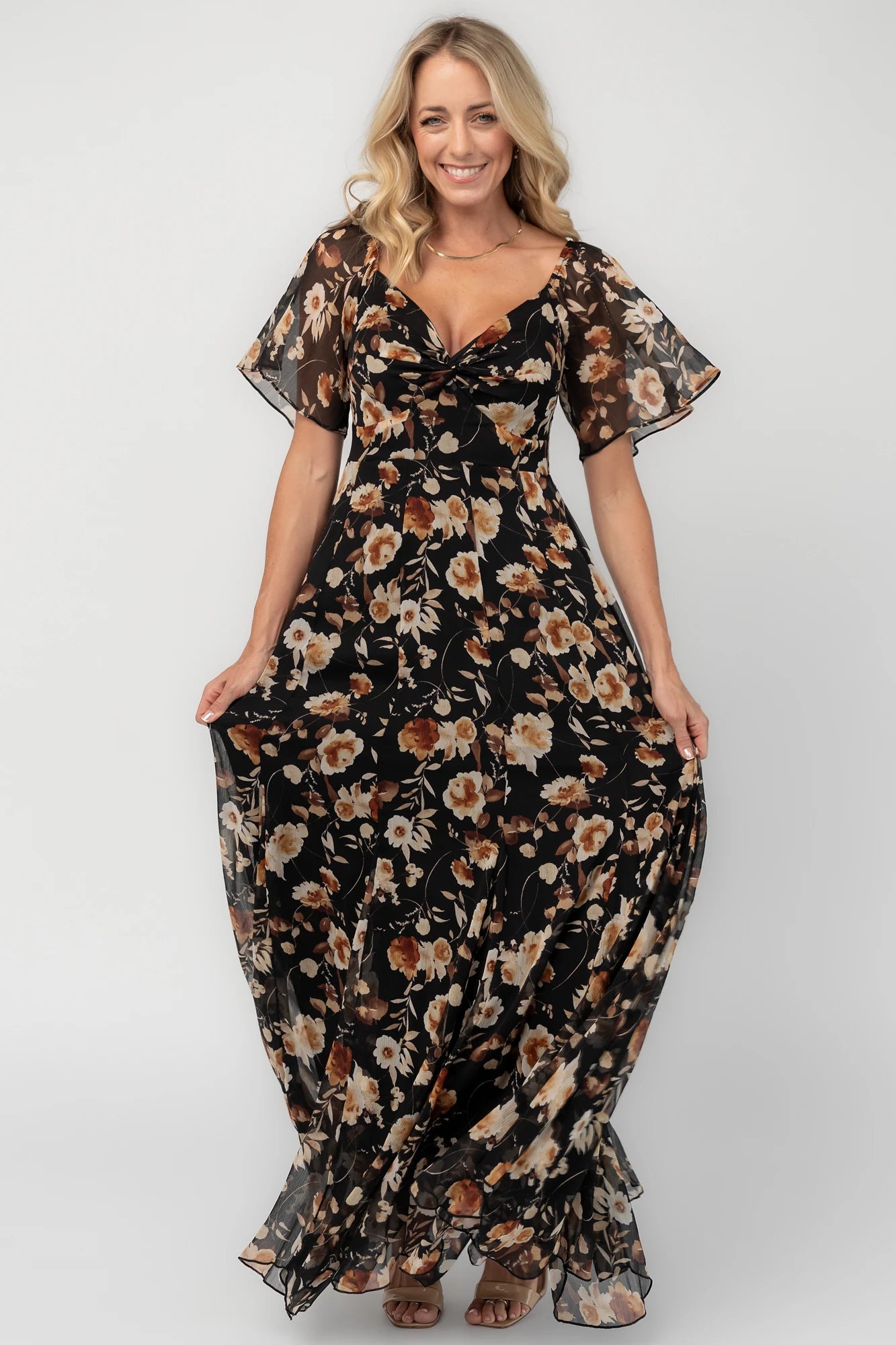 Black floral chiffon maxi dress with a sweetheart neckline, flutter sleeves, smocked back bodice, tiered skirt, and subtle gold foil detailing.