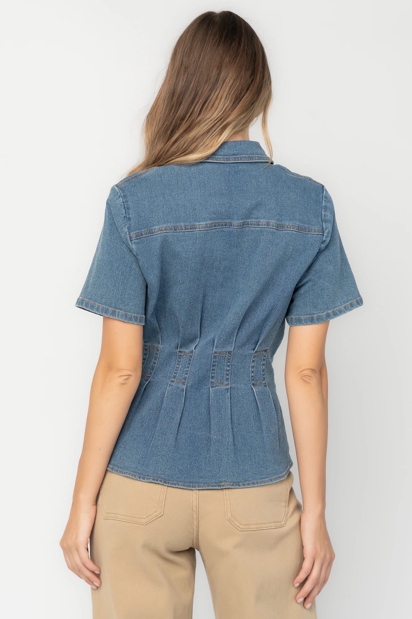 Medium wash stretch denim peplum top with a collared neckline, button-front closure, short sleeves, tailored seam detailing, and a flattering fitted silhouette.