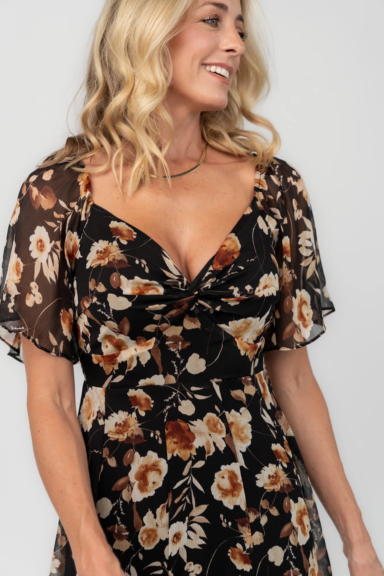 Black floral chiffon maxi dress with a sweetheart neckline, flutter sleeves, smocked back bodice, tiered skirt, and subtle gold foil detailing.