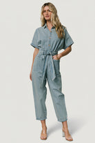 Back view of Mateo jumpsuit showing back patch pockets, tapered cuffed pant leg, and washed denim texture on model.