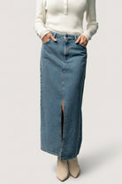 Model wearing Aleksa denim midi skirt styled with a sweater and booties, showing midi length, slit movement, and everyday styling.