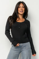 Front view of Leo Ribbed Henley Top in black on model, showing scoop neckline, henley-style buttons, and fitted ribbed hem (studio lighting).