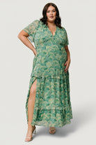 Side-angle of model in green floral chiffon maxi dress highlighting tiered ruffles, soft drape and the subtle leg slit for movement.