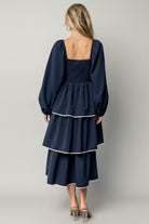 Model walking in navy Barcelona tiered midi dress showing movement of overlapping tiers and soft balloon sleeve silhouette.