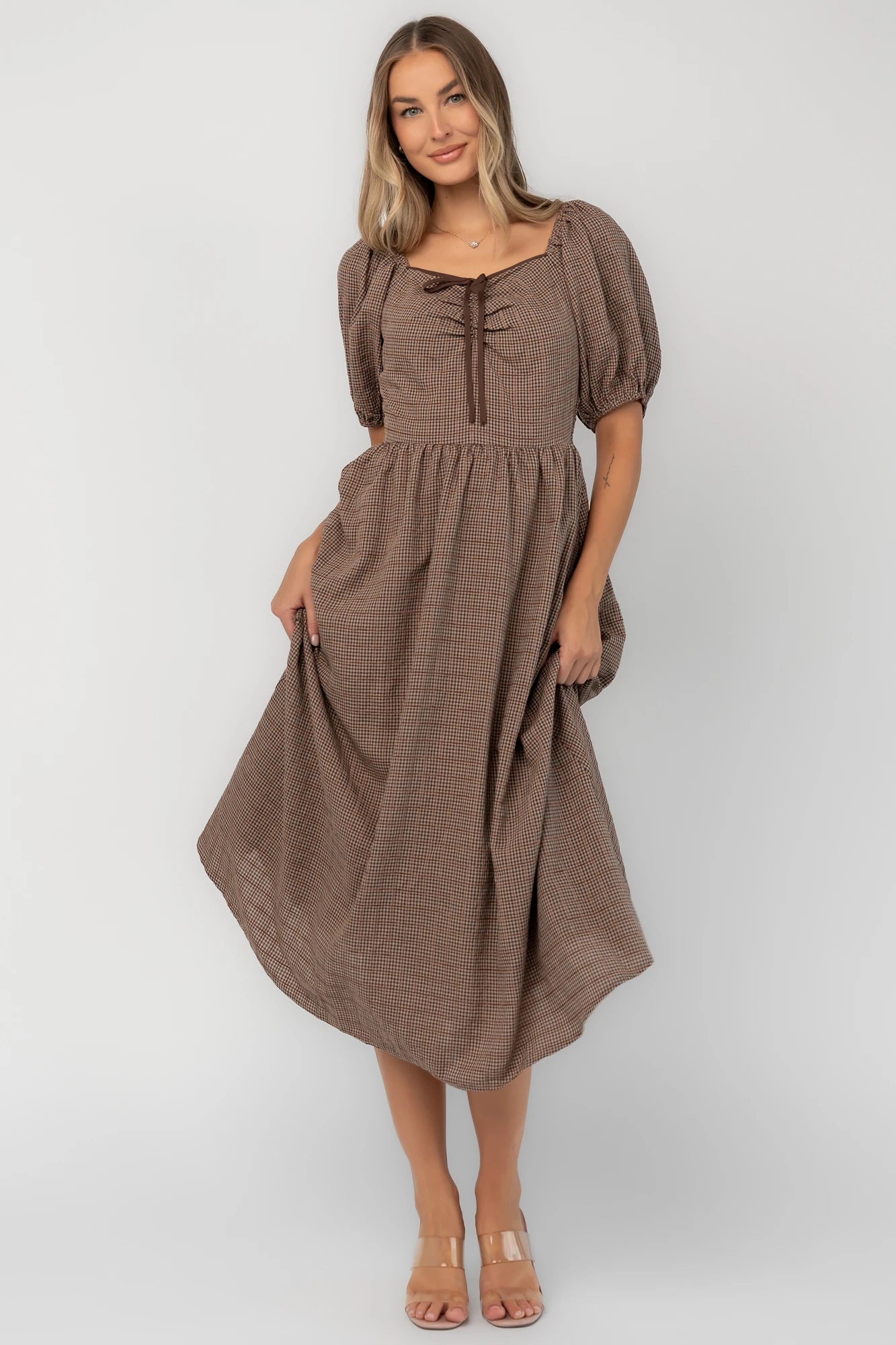 Mocha gingham midi dress with a square neckline, puff sleeves, smocked back, side pockets, and a flowing tiered skirt.