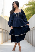 Close-up of the gathered center bust seam, decorative bow, and ivory accent trim on the navy Barcelona tiered dress.
