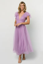 Full-length view of Annabella Tulle Midi Dress in lavender on model, highlighting V-neckline, ruffle sleeves, removable waist tie, and layered tulle skirt.
