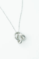 White background of  a delicate silver-tone necklace featuring an interlocking infinity knot pendant suspended from a fine chain. 