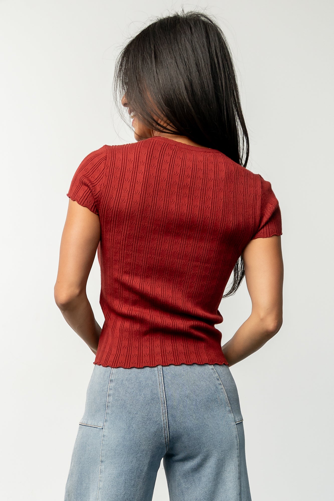 Casual styling shot of Penny Pointelle top in brick paired with high-waist jeans, showing overall fit and hem scallop detail.