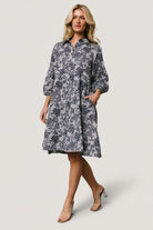 Front view of Dakota navy botanical babydoll dress on model, showing full button-front, tiered short skirt and roomy side pockets.