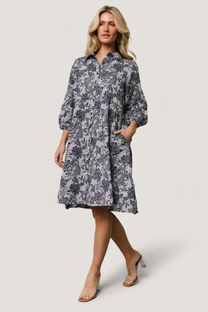 Front view of Dakota navy botanical babydoll dress on model, showing full button-front, tiered short skirt and roomy side pockets.