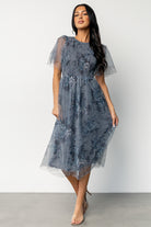Model wearing Josie Tulle Midi Dress in dusty blue floral, angled view showing round neckline, keyhole closure at back, and midi skirt movement.